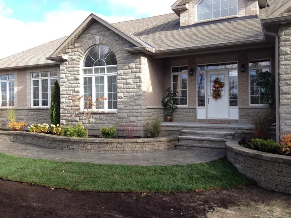 Design ideas for a mid-sized traditional front yard stone retaining wall landscape in Ottawa.