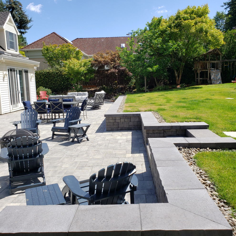 Imagen de jardín clásico renovado grande en verano en patio trasero con muro de contención, exposición total al sol, adoquines de hormigón y con madera