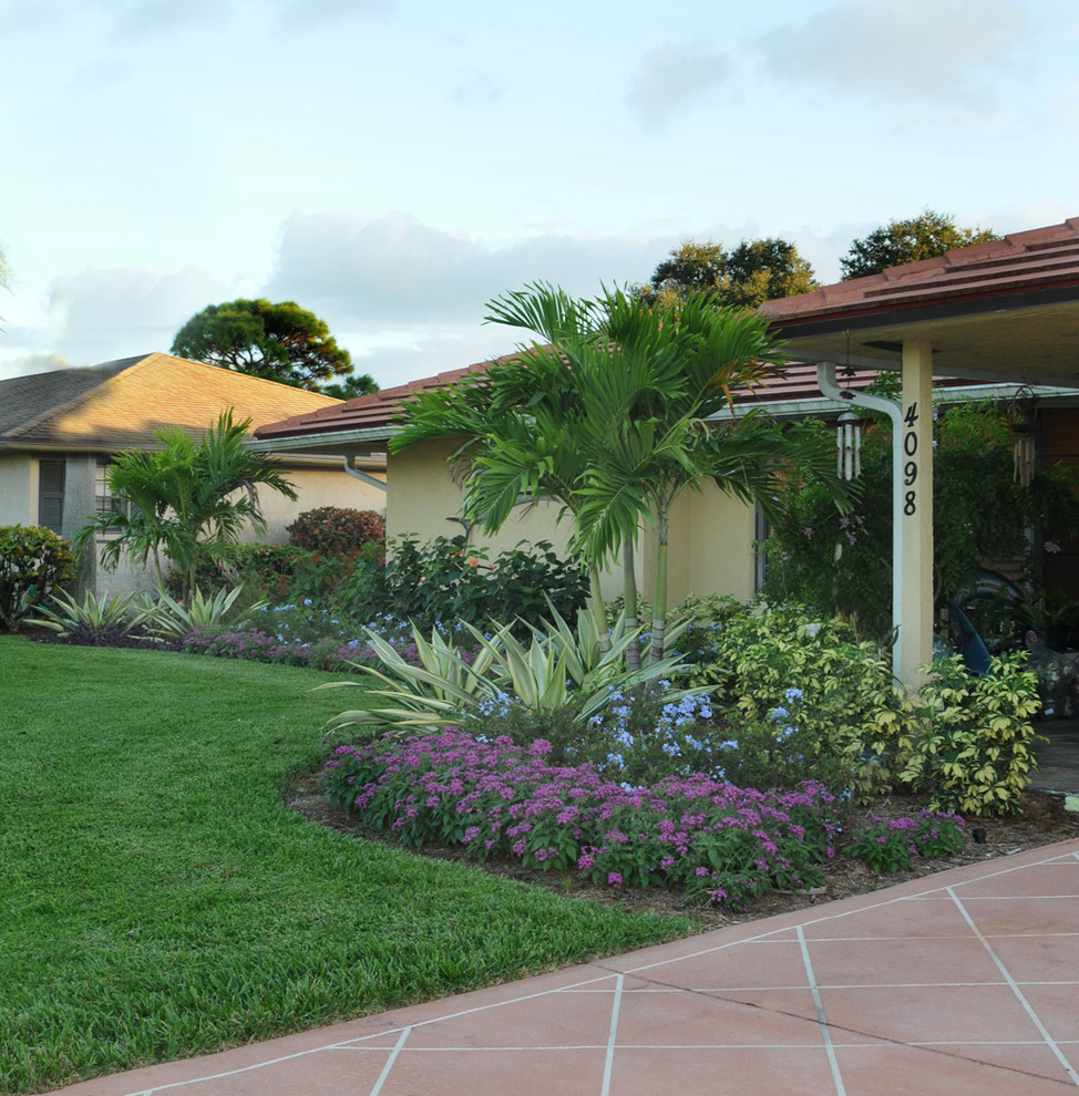 Foto på en tropisk formell trädgård i full sol framför huset på sommaren, med en trädgårdsgång och marksten i betong