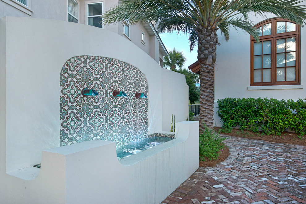 Photo of a large mediterranean front driveway partial sun garden in Miami with a water feature and brick paving.