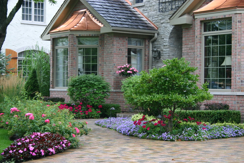 Exempel på en klassisk trädgård framför huset, med marksten i tegel och utekrukor