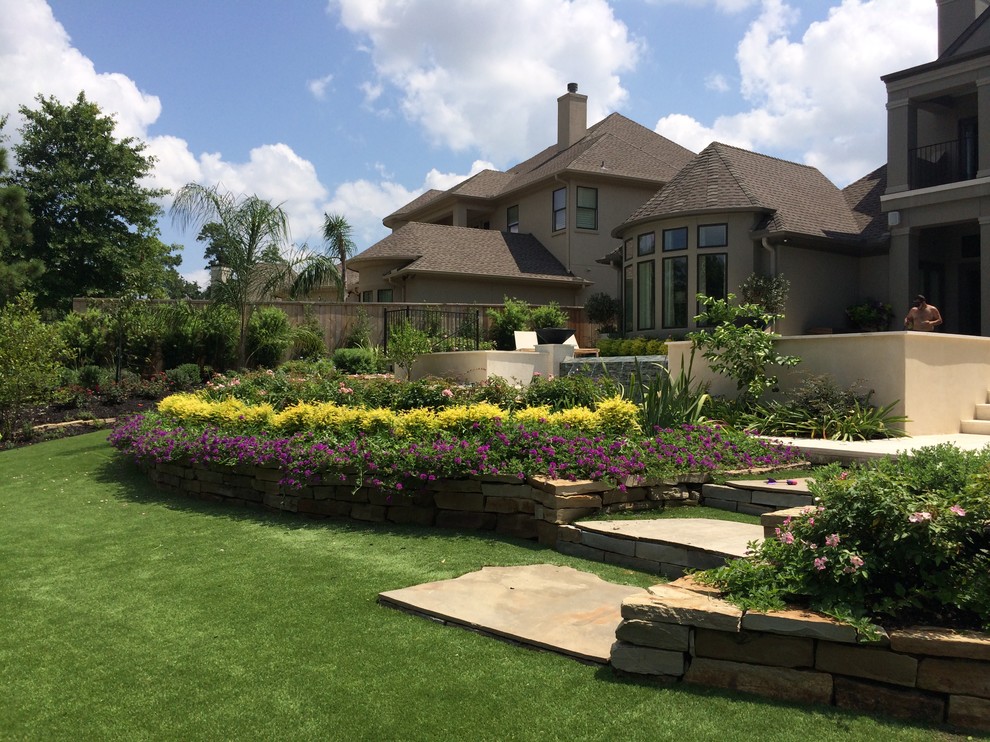 Large mediterranean back fully shaded garden for summer in Houston with a retaining wall and natural stone paving.