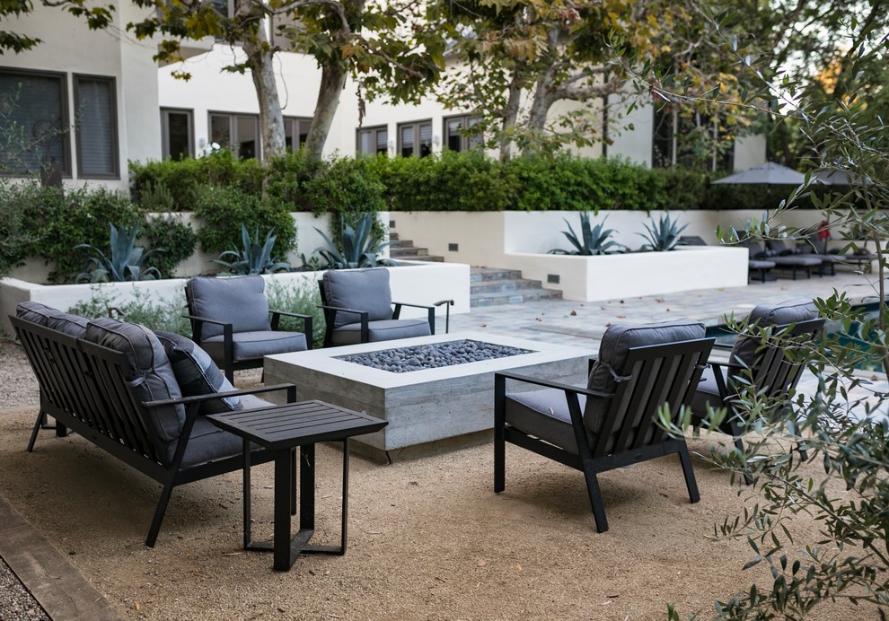 Large mediterranean back xeriscape partial sun garden in Los Angeles with a fire feature and gravel.