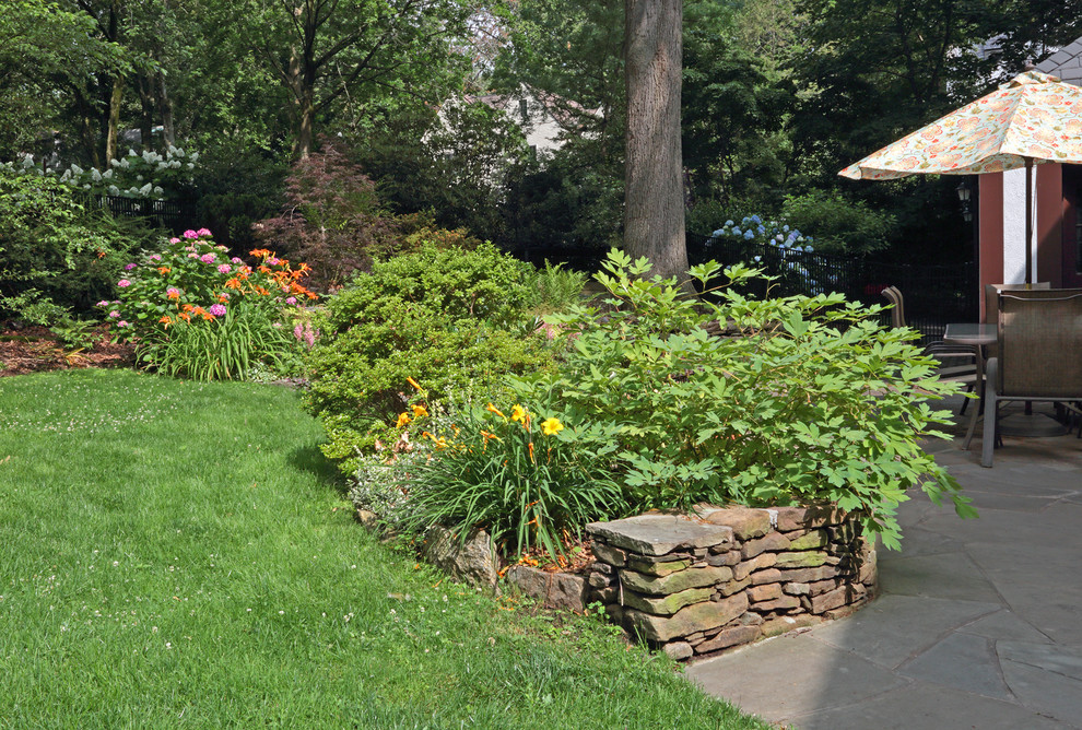 Esempio di un grande giardino tradizionale dietro casa in estate con un muro di contenimento e pavimentazioni in pietra naturale