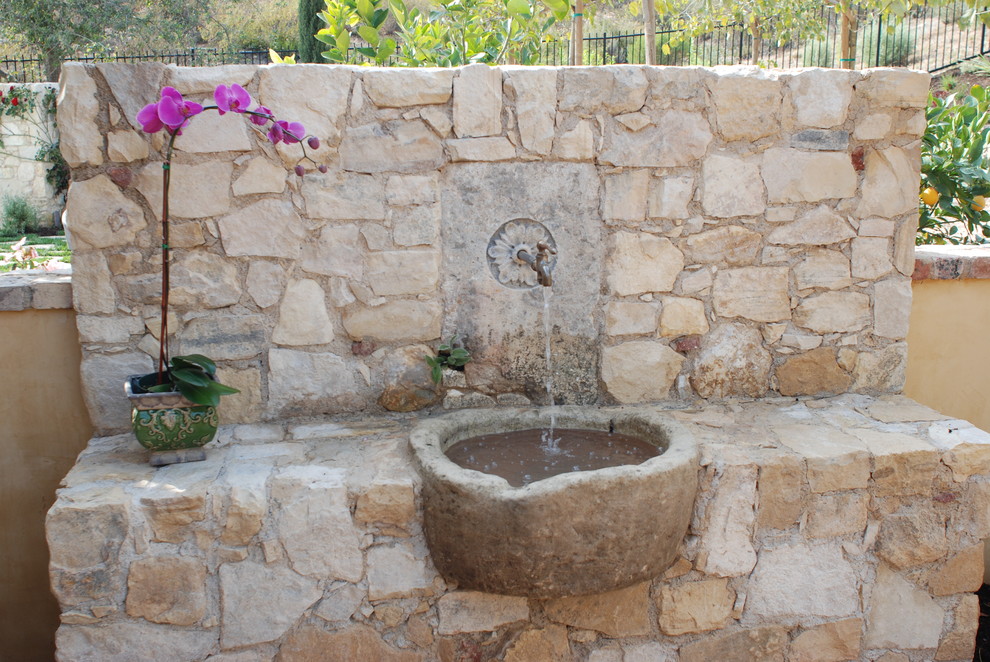 Immagine di un grande giardino mediterraneo esposto a mezz'ombra dietro casa con fontane e pavimentazioni in pietra naturale