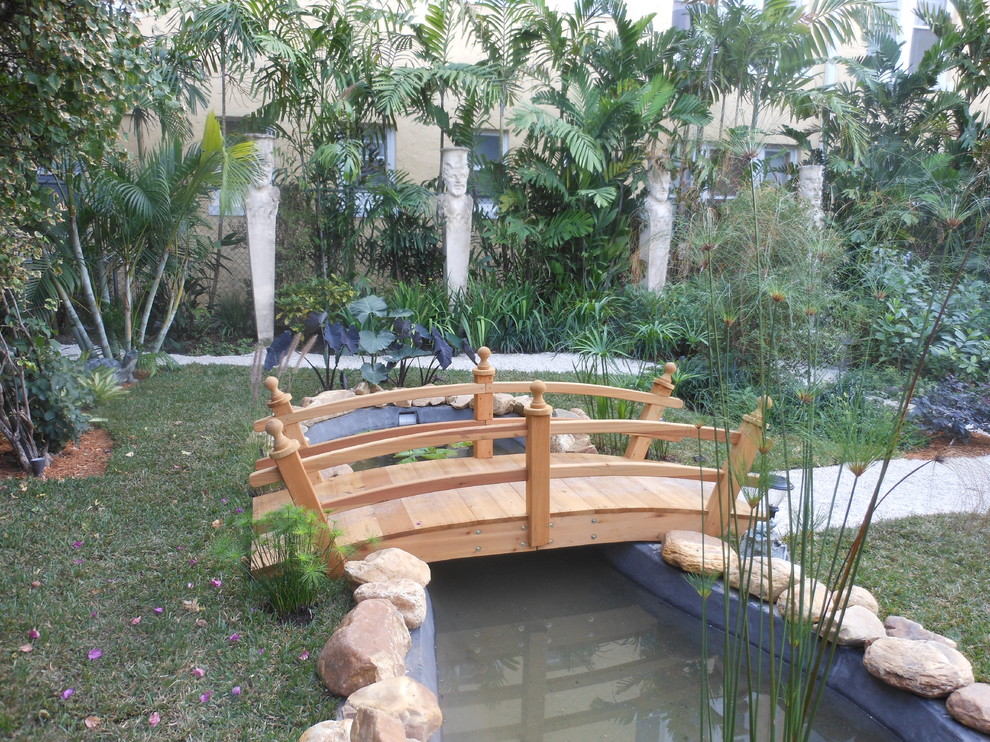 Modelo de jardín tropical grande en patio trasero con huerto, exposición parcial al sol y adoquines de ladrillo