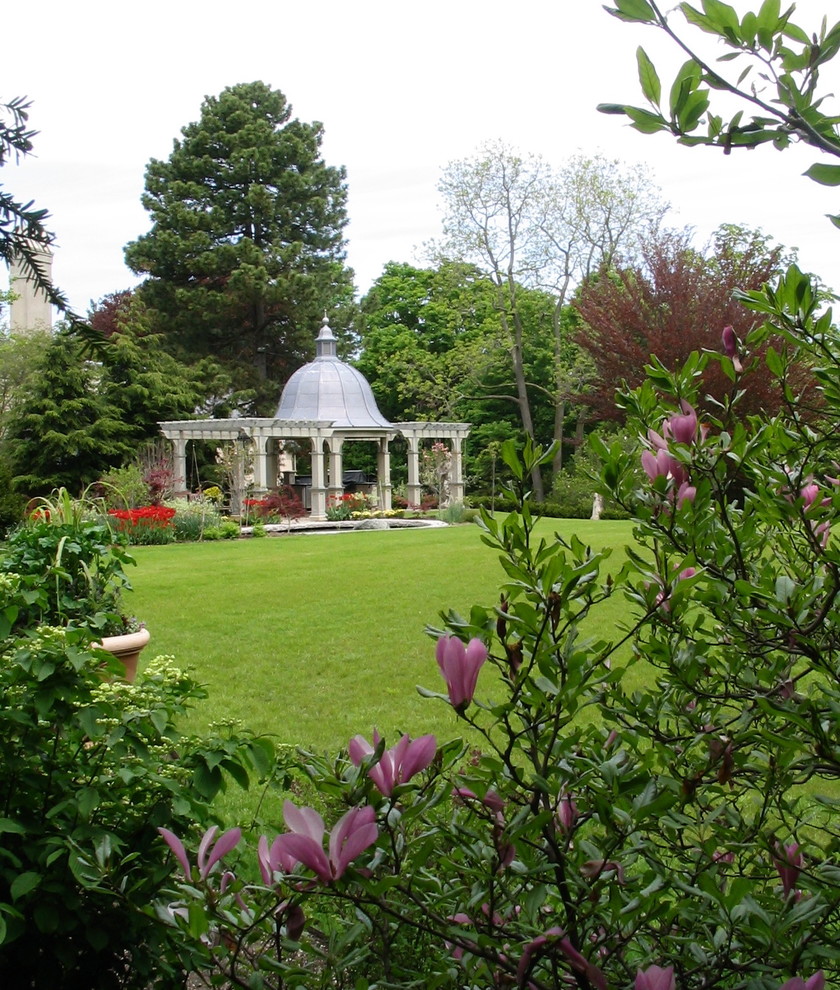Imagen de jardín clásico grande en verano en patio trasero con jardín francés, fuente, exposición parcial al sol y adoquines de piedra natural