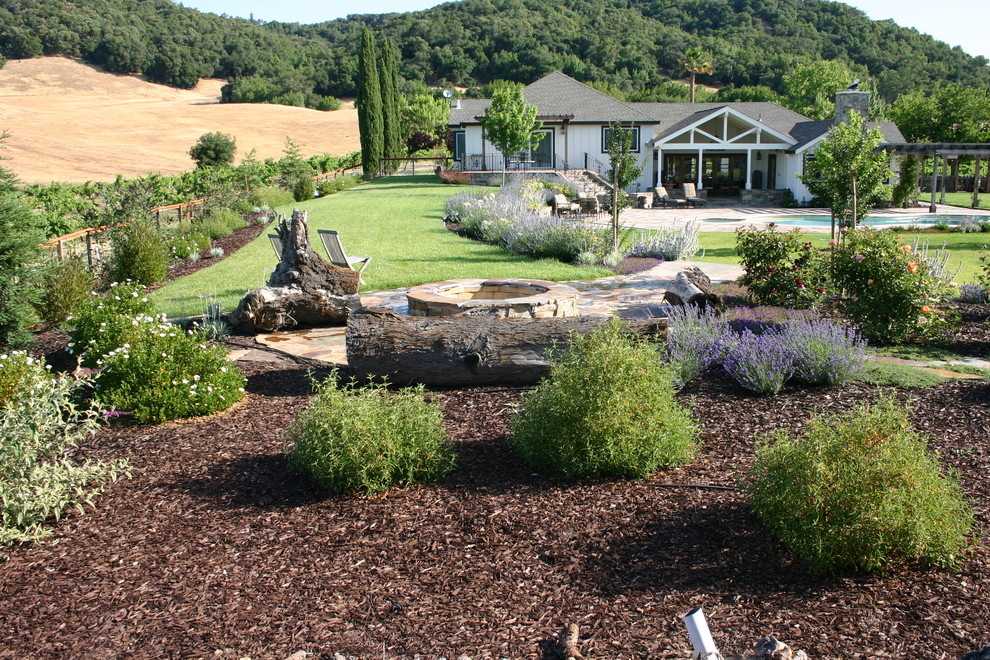 Стильный дизайн: большой солнечный участок и сад на заднем дворе в современном стиле с местом для костра, хорошей освещенностью и покрытием из каменной брусчатки - последний тренд
