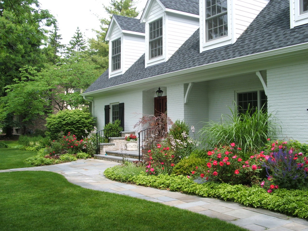 На фото: участок и сад на переднем дворе в классическом стиле с покрытием из каменной брусчатки и клумбами с