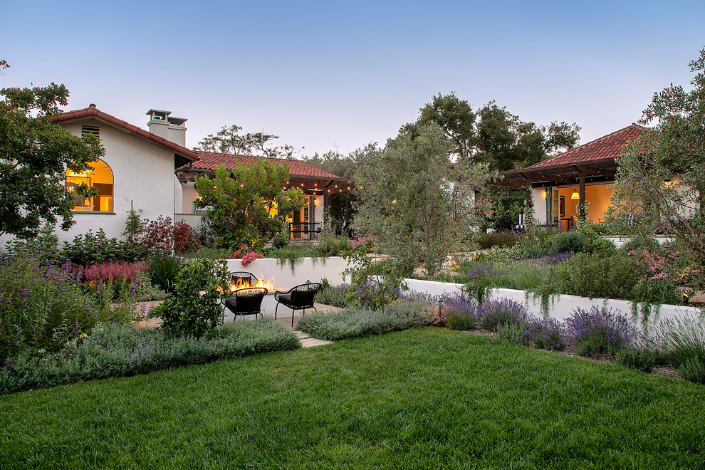 Großer Mediterraner Garten hinter dem Haus mit Feuerstelle, direkter Sonneneinstrahlung und Pflastersteinen in Santa Barbara