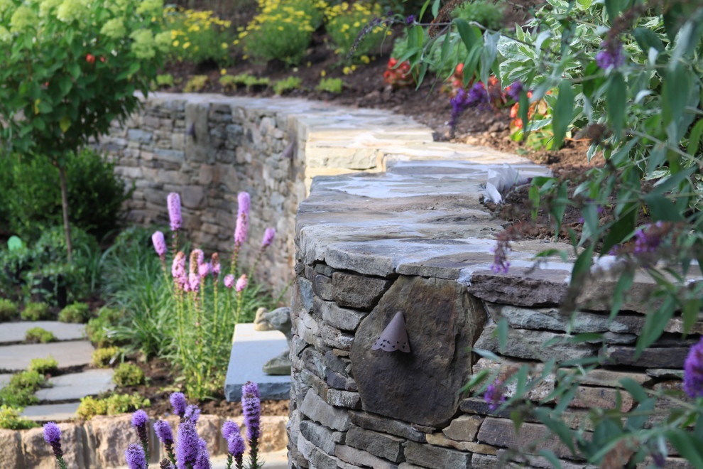 Modelo de jardín tradicional grande en verano en patio trasero con exposición total al sol, adoquines de piedra natural y muro de contención