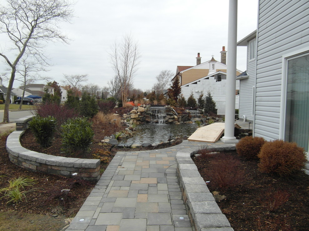 This is an example of a medium sized coastal back partial sun garden for summer in New York with a water feature and concrete paving.