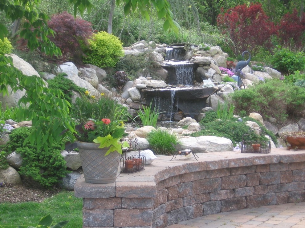 Imagen de jardín exótico en verano en patio trasero con jardín francés, estanque, exposición total al sol y adoquines de piedra natural