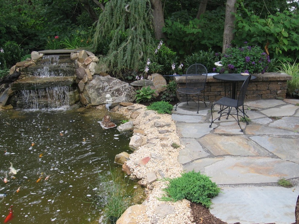 World-inspired side xeriscape partial sun garden for summer in New York with a pond and natural stone paving.