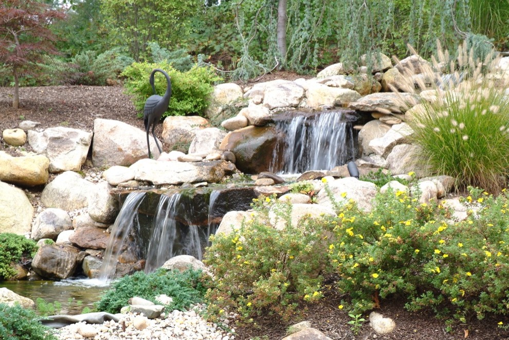 Ejemplo de jardín de secano tropical en verano en ladera con estanque, exposición total al sol y adoquines de piedra natural