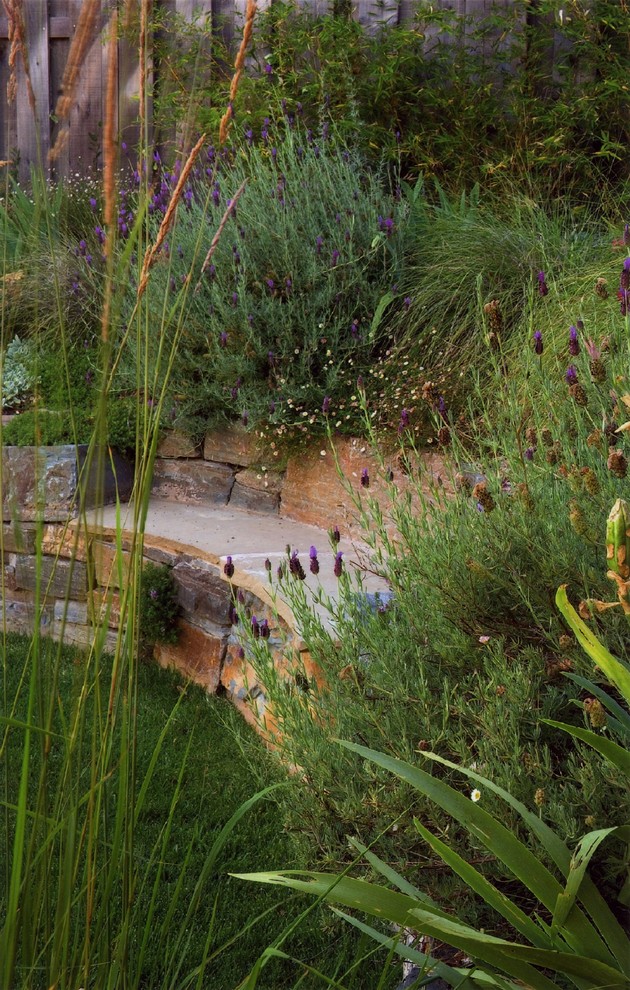 Réalisation d'un jardin arrière bohème de taille moyenne et au printemps avec un mur de soutènement, une exposition ensoleillée et des pavés en pierre naturelle.