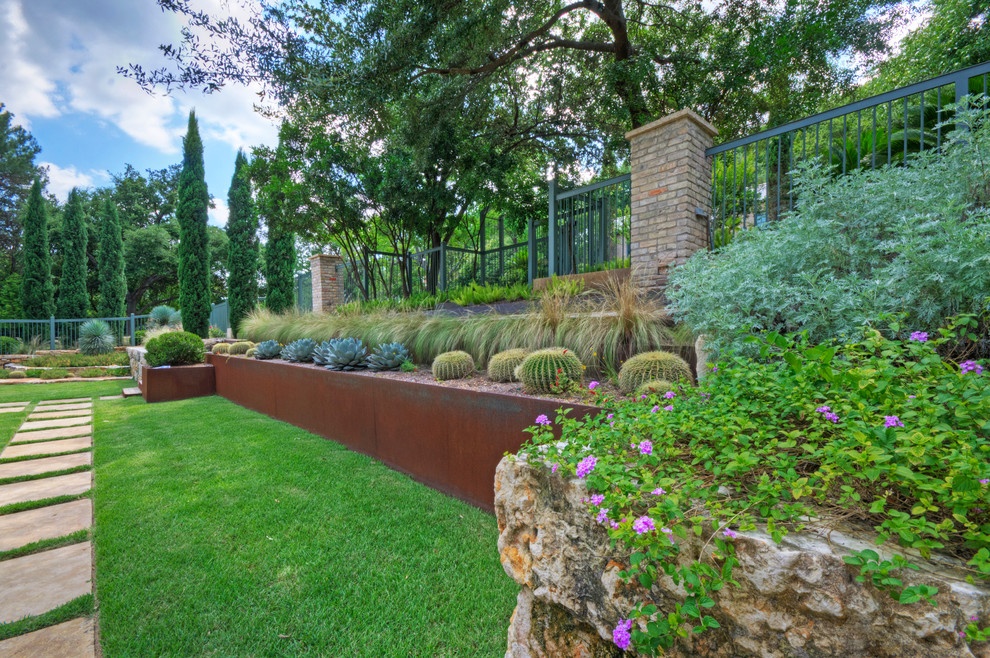 Inspiration for a large modern front xeriscape full sun garden for spring in Austin with a retaining wall and natural stone paving.