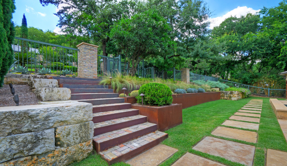 Photo of a large modern front xeriscape full sun garden for spring in Austin with a retaining wall and natural stone paving.