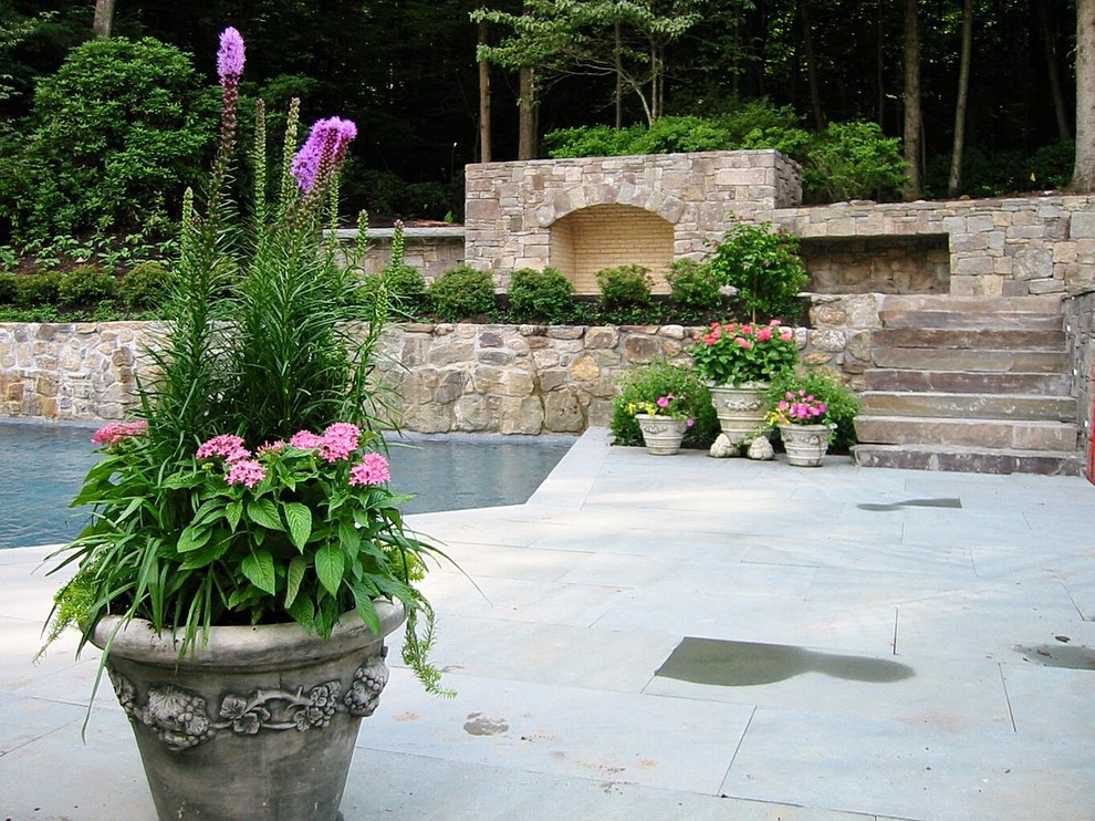 Foto di un grande giardino formale tradizionale esposto in pieno sole dietro casa in primavera con un muro di contenimento e pavimentazioni in pietra naturale