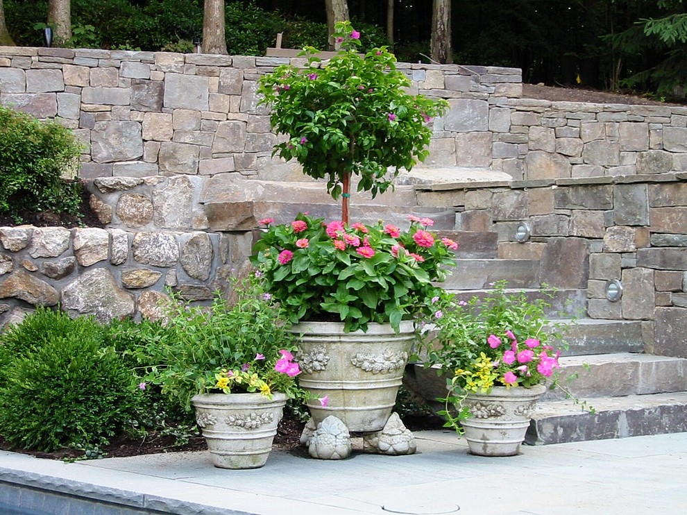 Idee per un grande giardino formale classico esposto in pieno sole dietro casa in primavera con un muro di contenimento e pavimentazioni in pietra naturale