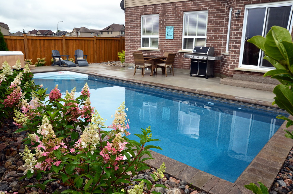 Modelo de piscina con fuente clásica de tamaño medio en patio trasero con adoquines de hormigón