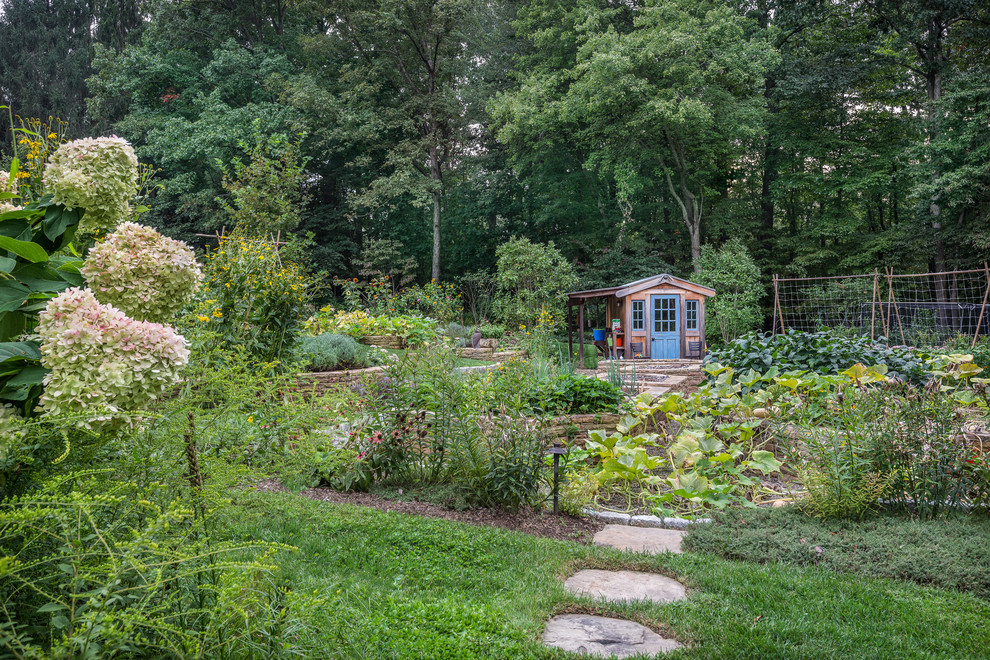 Bild på en stor lantlig formell trädgård i full sol längs med huset på sommaren, med en köksträdgård och naturstensplattor