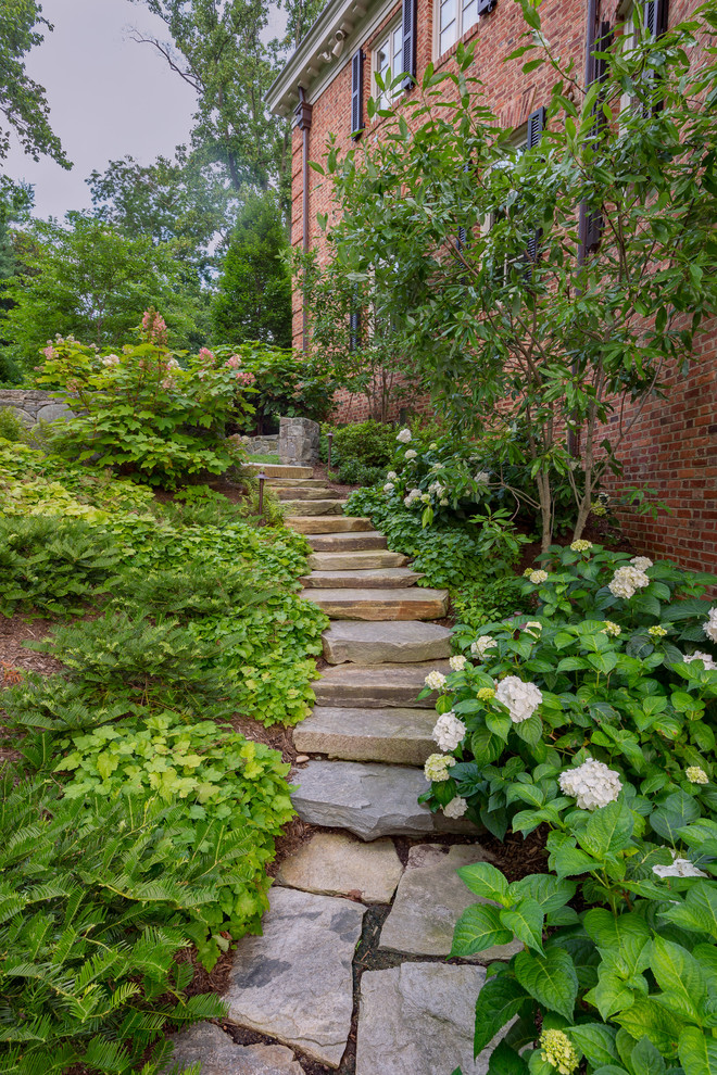 Exempel på en klassisk trädgård längs med huset, med en trädgårdsgång och naturstensplattor