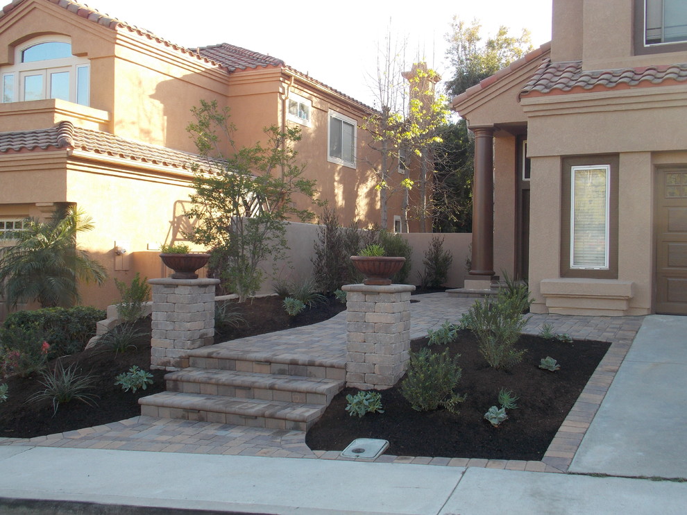 This is an example of a mediterranean drought-tolerant and partial sun front yard concrete paver landscaping in Orange County for spring.