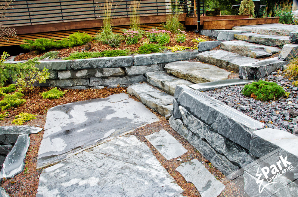 Inspiration for a large contemporary sloped formal garden in Calgary with a retaining wall and natural stone paving.