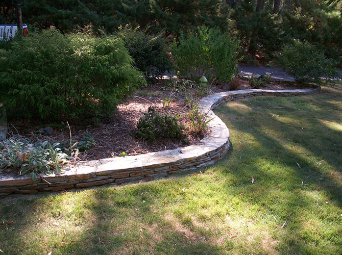 Ejemplo de jardín tradicional de tamaño medio en otoño en patio trasero con muro de contención, exposición reducida al sol y adoquines de piedra natural