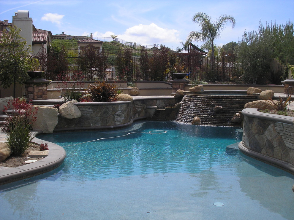 Exempel på en stor klassisk pool på baksidan av huset, med naturstensplattor