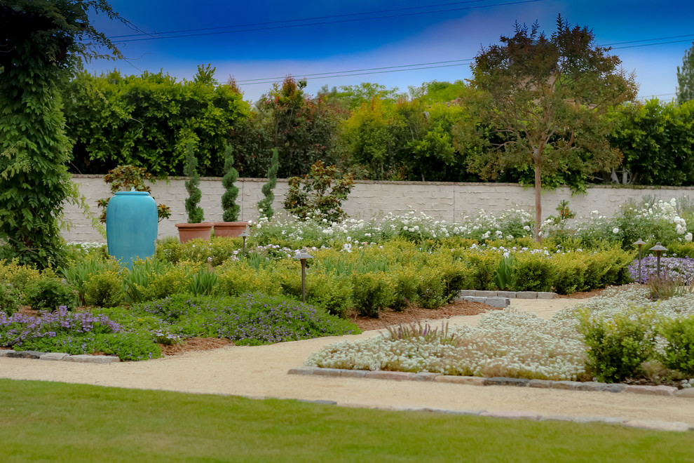 Foto di un ampio giardino formale mediterraneo esposto in pieno sole dietro casa in primavera con un ingresso o sentiero e graniglia di granito