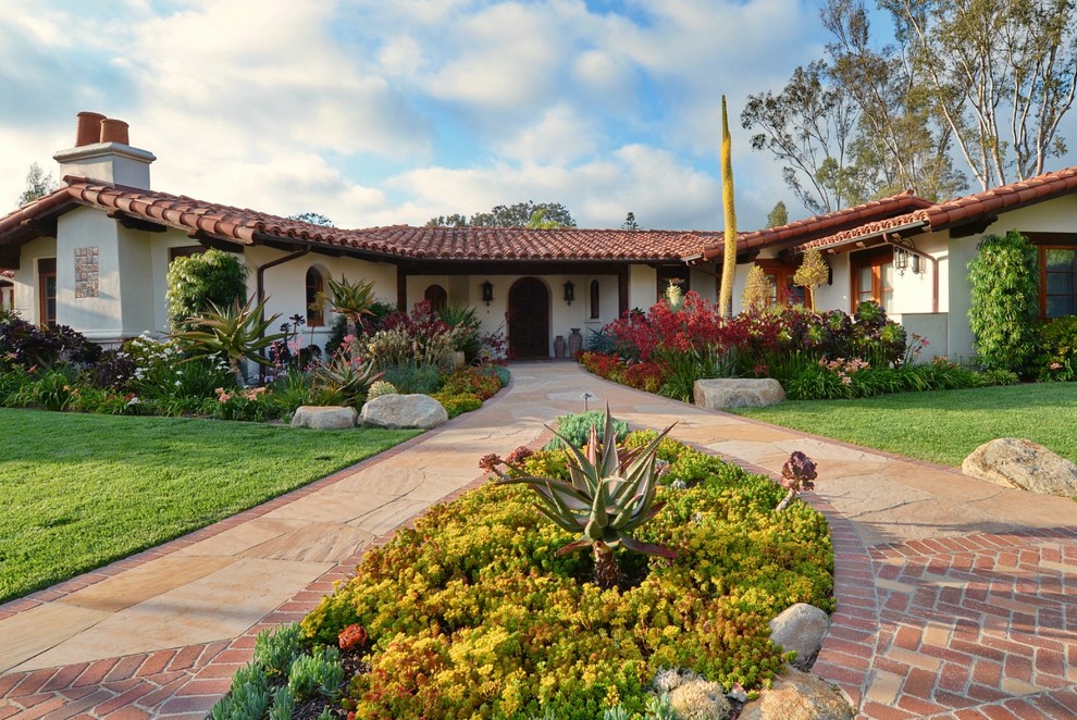 Expansive mediterranean front driveway full sun garden for spring in San Diego with a garden path and natural stone paving.