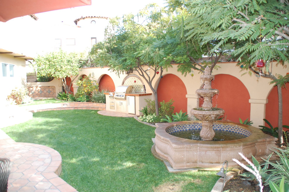 This is an example of a large mediterranean back formal partial sun garden for spring in San Diego with a fire feature and brick paving.