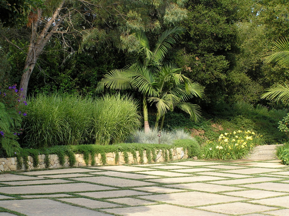 Bild på en stor tropisk uppfart i delvis sol framför huset, med marksten i betong