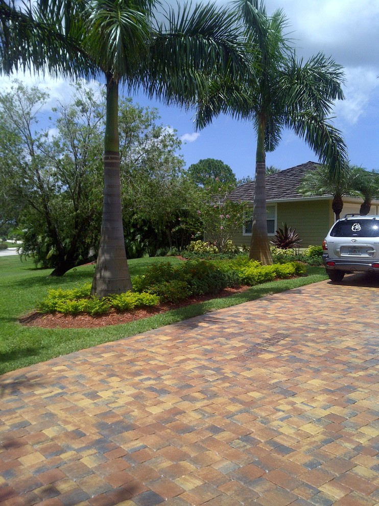 Large world-inspired front driveway full sun garden for summer in Miami with natural stone paving and a garden path.