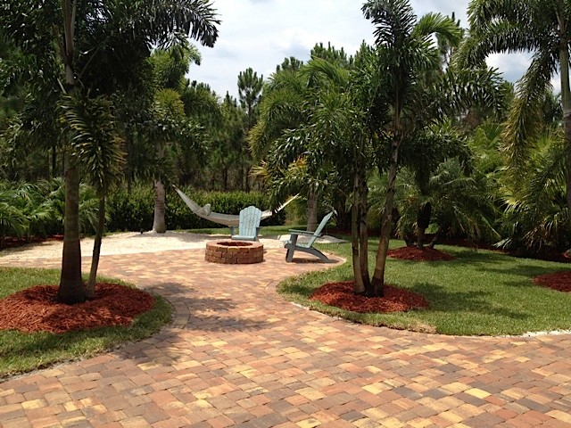 Diseño de acceso privado tropical de tamaño medio en verano en patio trasero con brasero, exposición total al sol y adoquines de ladrillo