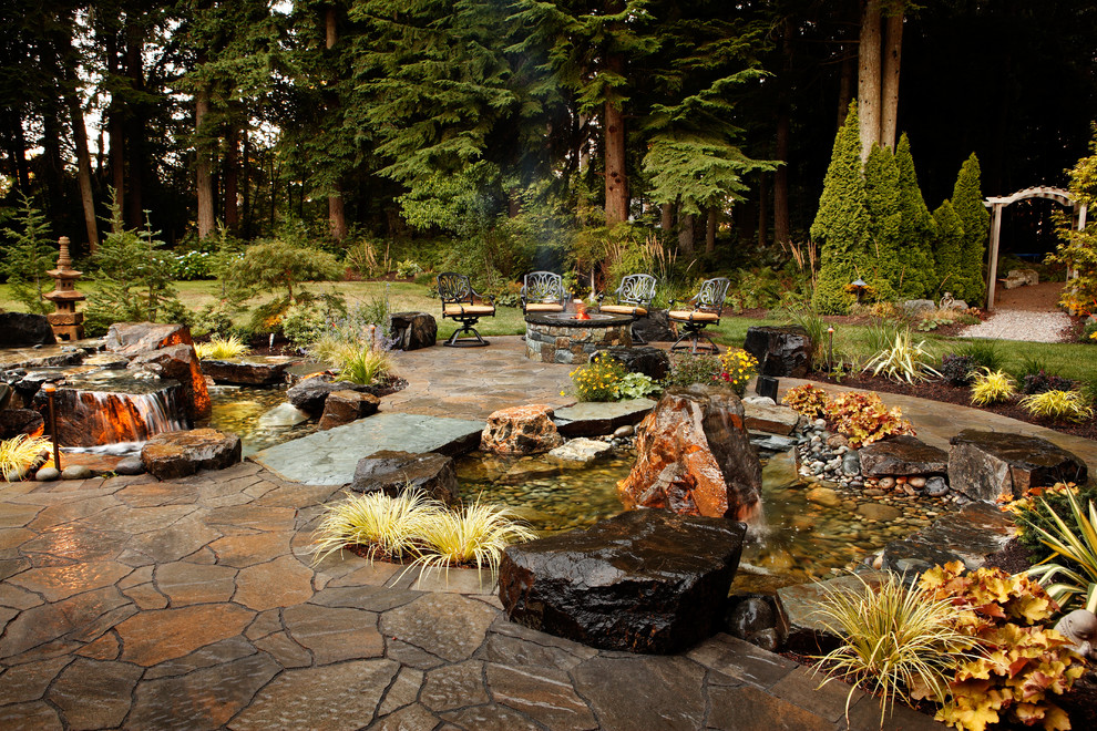 Klassisk inredning av en stor trädgård i full sol, med en fontän och naturstensplattor