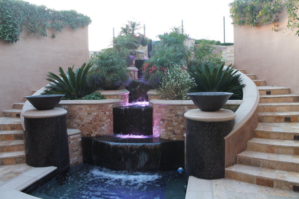 Medium sized mediterranean back full sun garden in Orange County with a water feature and natural stone paving.