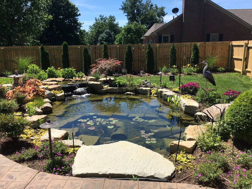 Modelo de jardín clásico grande en verano en patio trasero con jardín francés, estanque, exposición parcial al sol y adoquines de piedra natural