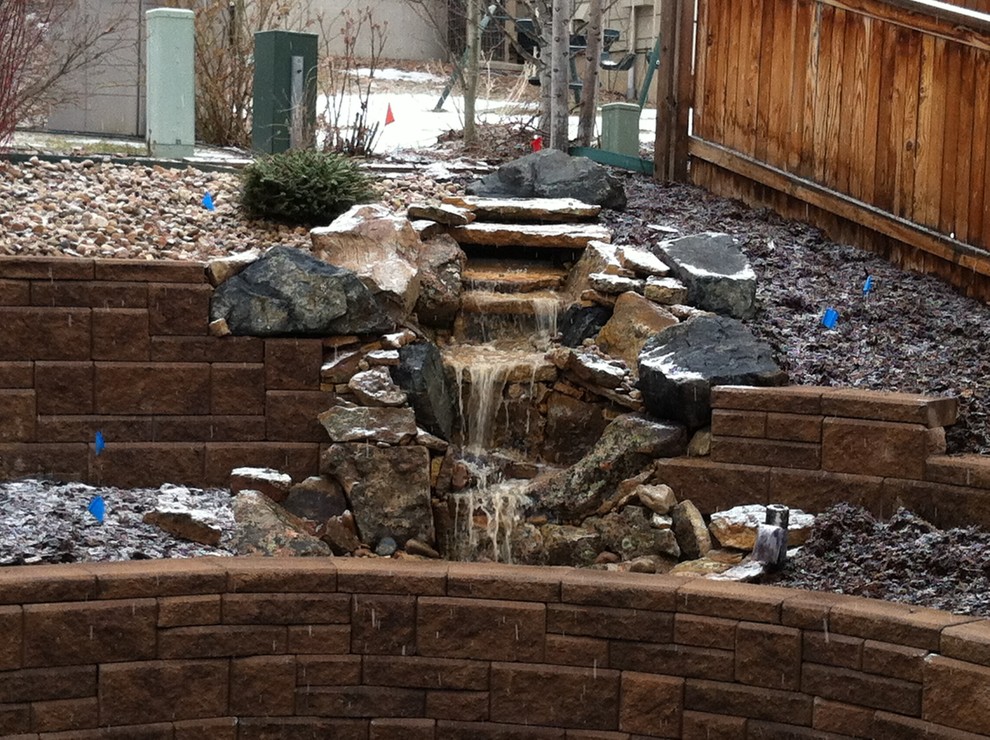 Inspiration for a sloped xeriscape garden in Denver with a waterfall and decorative stones.