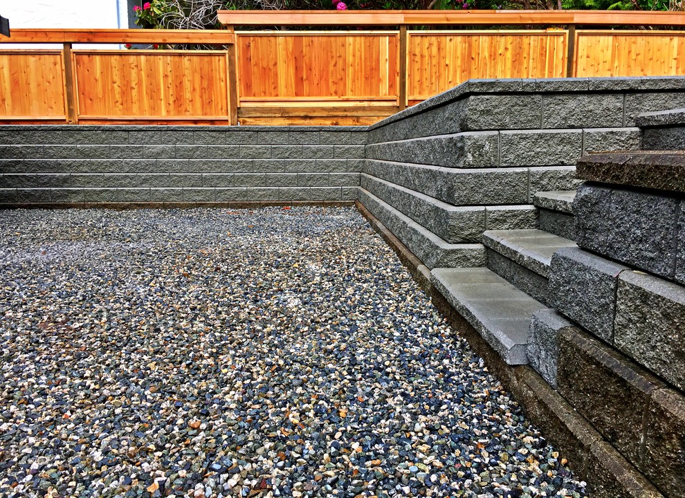 Modern back fully shaded garden in Vancouver with a retaining wall, gravel and a wood fence.