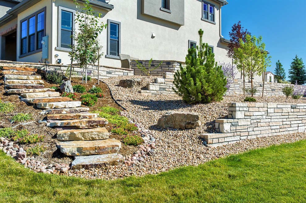 Cette image montre un grand jardin arrière design avec un mur de soutènement et des pavés en pierre naturelle.