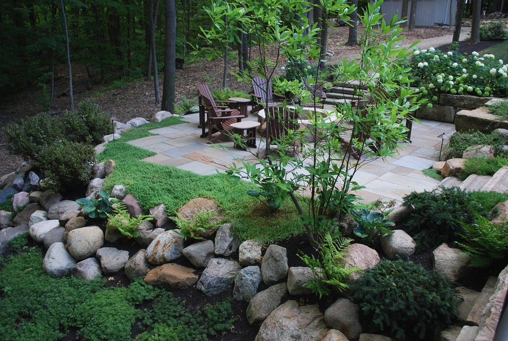 Cette photo montre un grand jardin arrière chic au printemps avec un mur de soutènement, une exposition ombragée et des pavés en pierre naturelle.