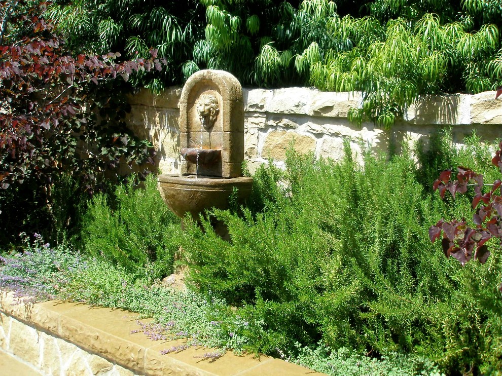 Foto di un giardino mediterraneo esposto in pieno sole con fontane e pavimentazioni in pietra naturale