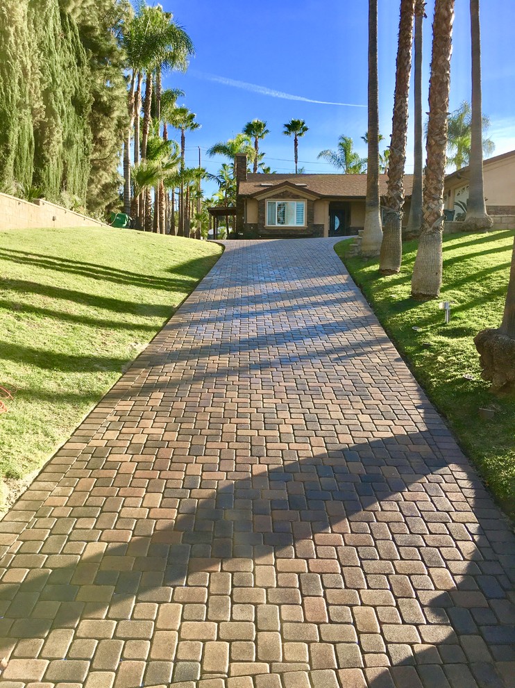 Photo of a large traditional front driveway partial sun garden in Orange County with a retaining wall and brick paving.