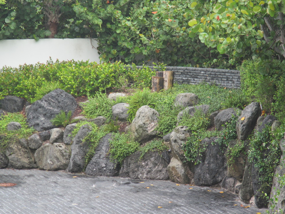 Medium sized world-inspired front driveway garden in Miami with natural stone paving and a retaining wall.