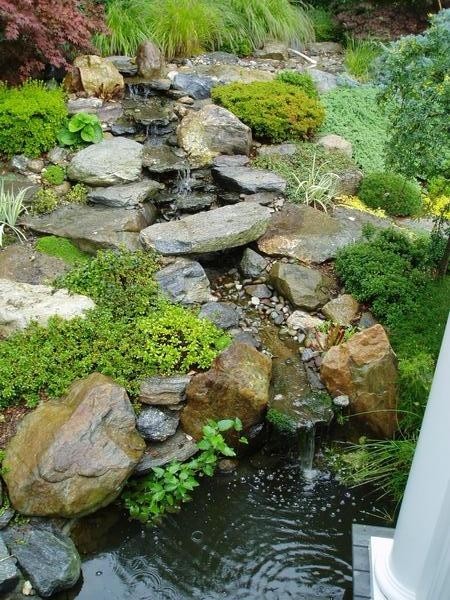 Ejemplo de jardín tradicional en ladera con fuente y adoquines de piedra natural