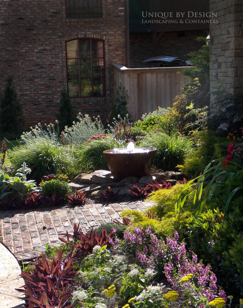 Imagen de jardín tradicional en verano en patio delantero con fuente, exposición total al sol y adoquines de ladrillo