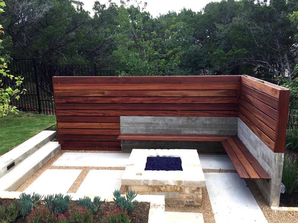 Halbschattiger Moderner Garten hinter dem Haus mit Feuerstelle und Betonboden in Austin